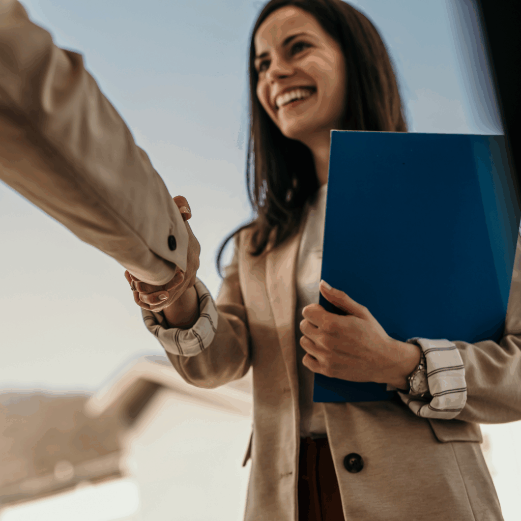 Woman smiling, holding paperwork and shaking hands at a job interview